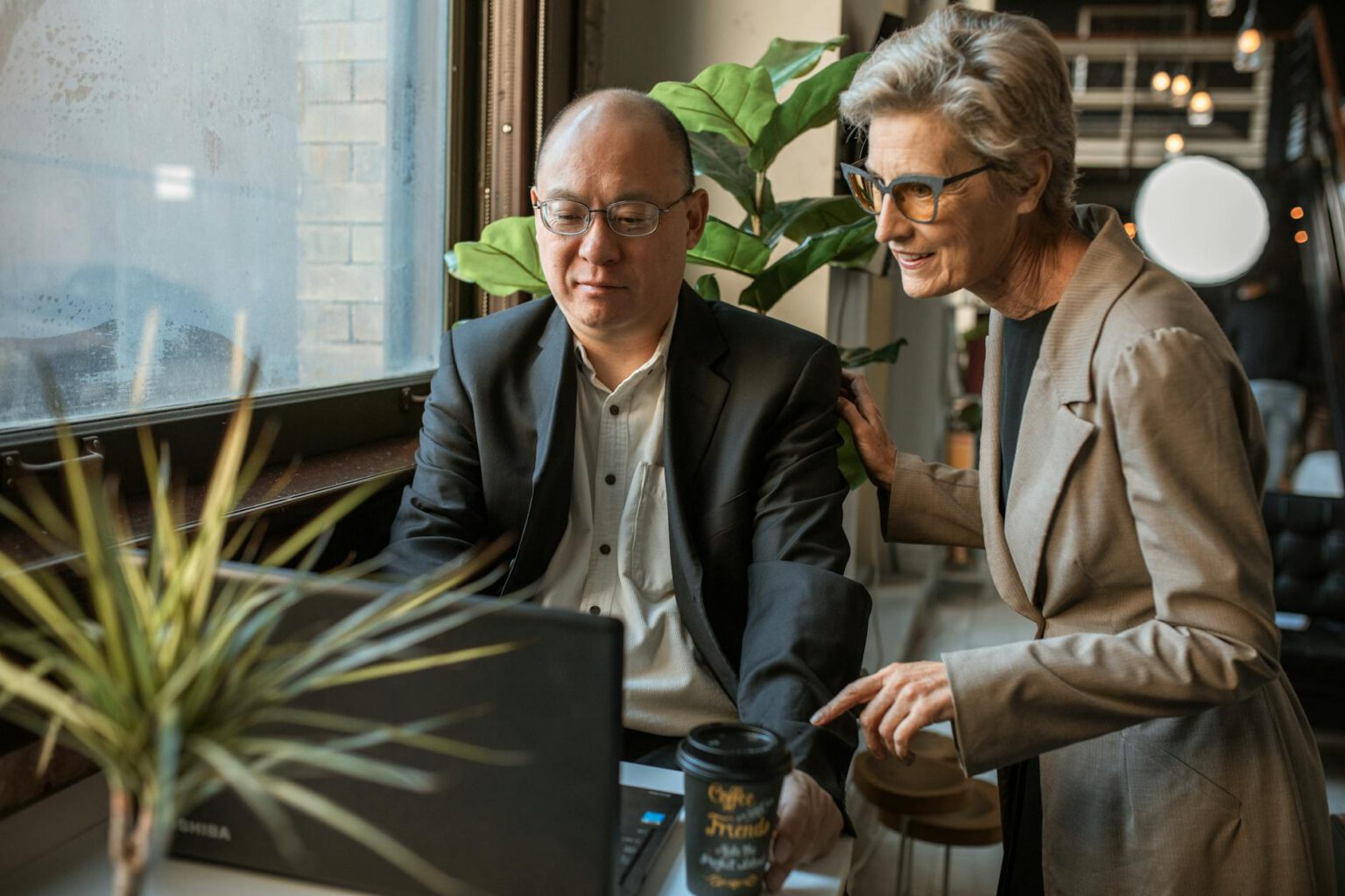 Two colleagues working together on a laptop in a modern office setting