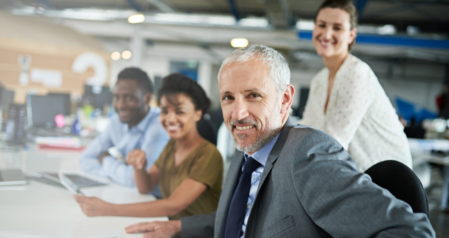 Senior team leader in modern office with diverse IT team in the background