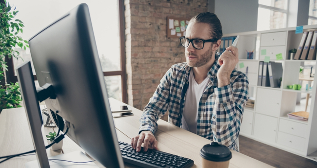 Man in glasses coding at a desktop computer in an open office