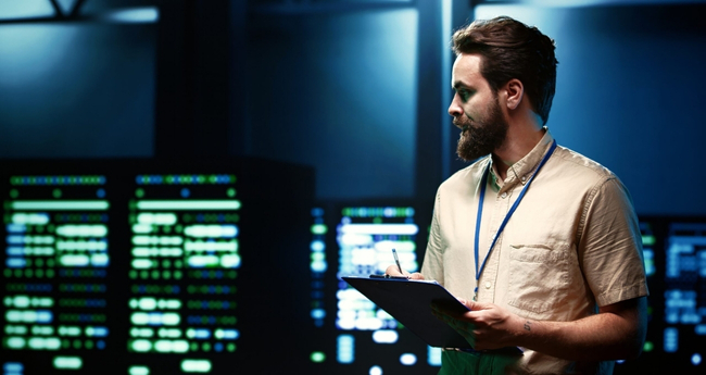 Bearded man with clipboard standing in front of server racks