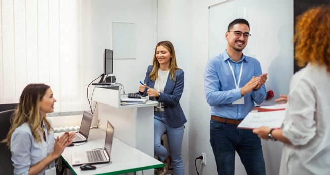 A team congratulates a colleague after completing an IT training session in a modern office
