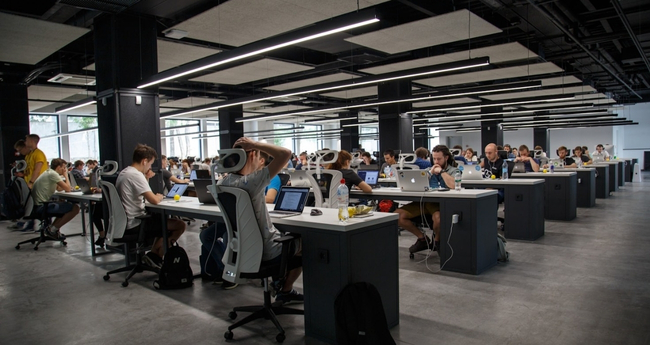 Open-plan office space filled with focused IT students at workstations