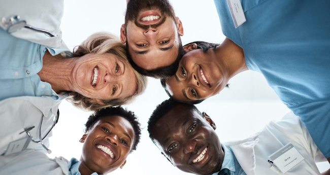Group of healthcare professionals smiling and standing in a circle, symbolizing teamwork and care
