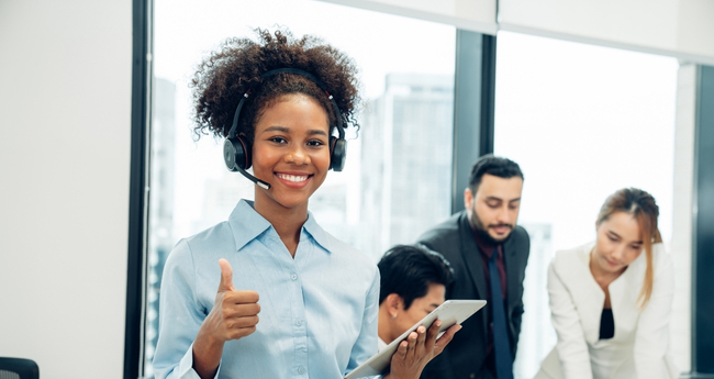 Happy female support agent using a tablet, giving a thumbs-up during customer interaction