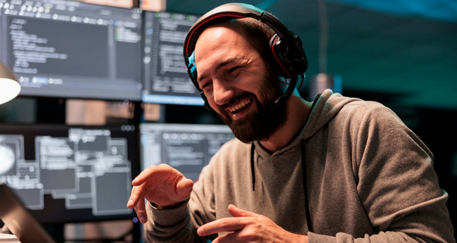 Smiling developer with headset in front of multiple screens during remote IT support session