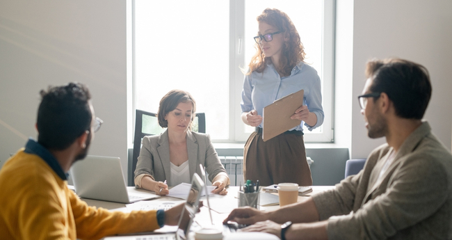 Group of IT professionals working together around a table, with one standing to lead the discussion in a tech-focused work environment