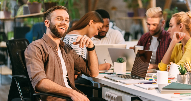 A man working at a desk with colleagues, all using laptops during a collaborative session
