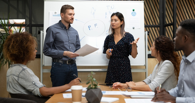 Two professionals presenting IT and workforce solutions to colleagues in a collaborative office setting