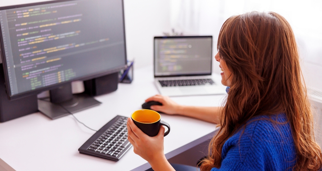 Female software developer working on code with laptop and desktop screen