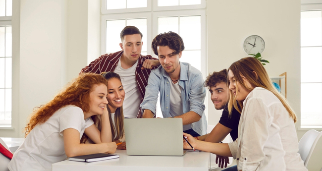 A group of young professionals gathered around a laptop during a tech project collaboration