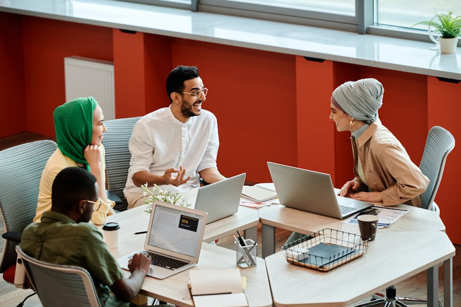 A group of diverse coworkers engaging in a collaborative discussion with laptops in a modern office setting