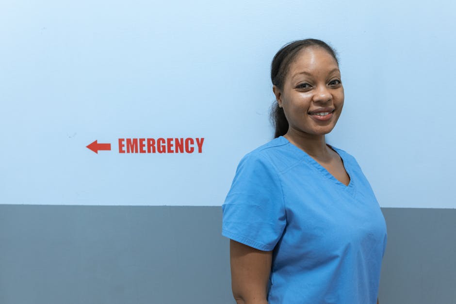 Happy healthcare worker in scrubs standing near an emergency room sign in a modern hospital